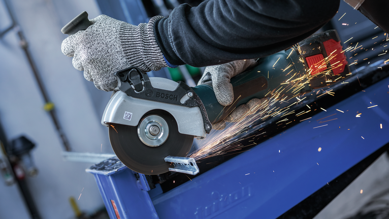 Person wearing safety equipment uses an angle grinder to cut metal, creating sparks.
