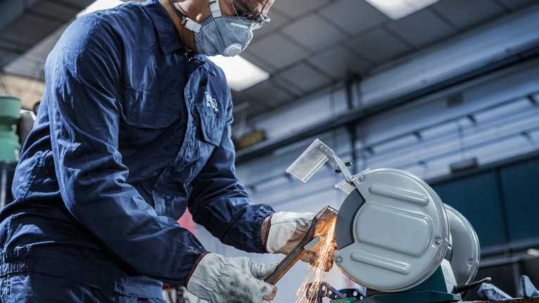Person wearing safety equipment uses a metal cutting saw to cut a pipe, producing sparks.