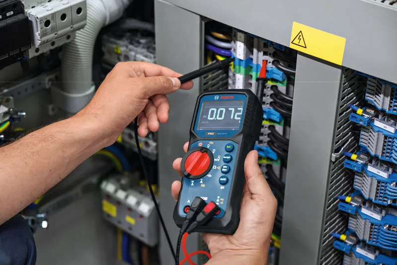 Person testing electrical panel with a digital multimeter.
