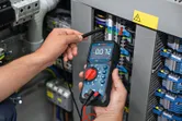 Person testing electrical panel with a digital multimeter.