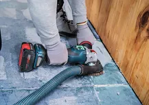 A person wearing safety equipment sands a concrete floor near a wooden wall.