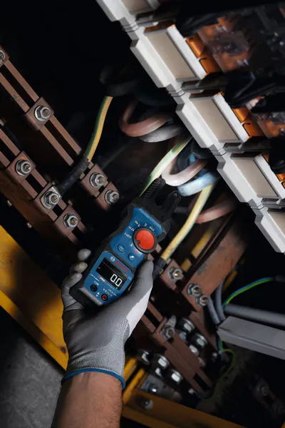 A person wearing safety equipment uses a fork meter to check electrical wiring.