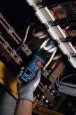 A person wearing safety equipment uses a fork meter to check electrical wiring.