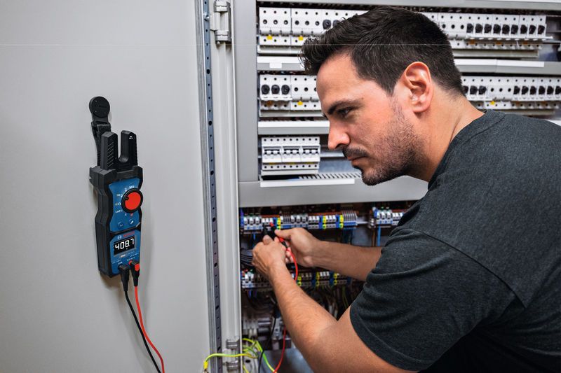 A person tests electrical connections in a control cabinet using a digital multimeter.