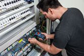 A person measures electrical values in a control panel using a fork meter.
