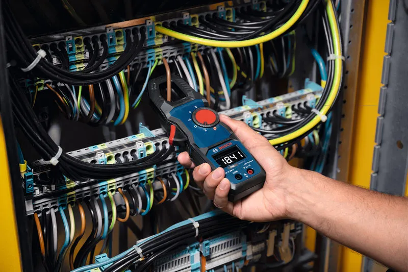 A person uses a clamp meter to measure voltage inside an electrical panel.