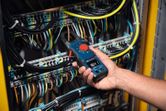 A person uses a clamp meter to measure voltage inside an electrical panel.