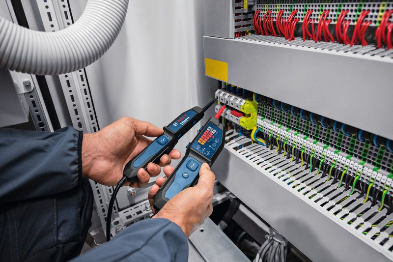 Person wearing safety equipment uses a voltage tester on an electrical panel.