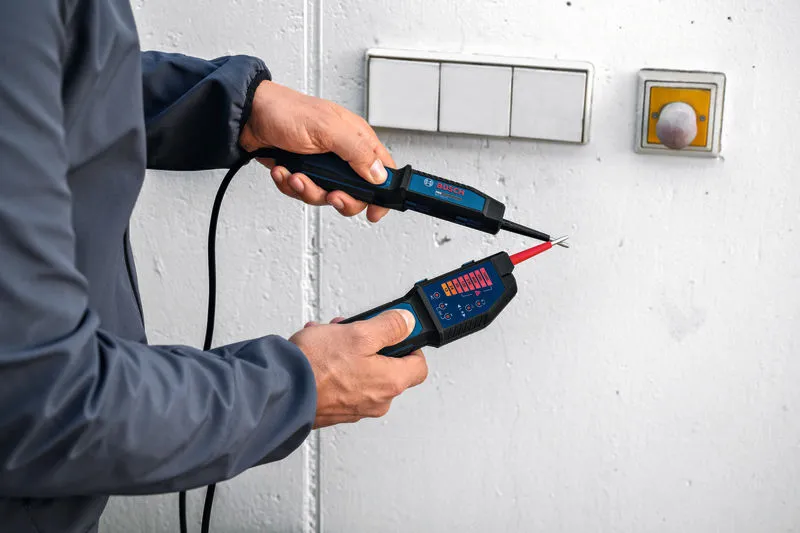 Person using a voltage tester to check electrical wires on a wall near switches.