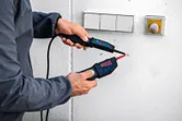 Person using a voltage tester to check electrical wires on a wall near switches.