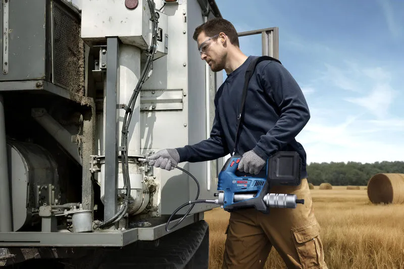 A person wearing safety equipment uses a power tool to service farm machinery in a field.