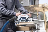 A person uses a cordless circular saw to cut wood outdoors.