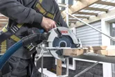 A person wearing safety equipment cuts wood with a cordless circular saw on scaffolding.