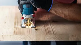 Person wearing safety equipment uses a jigsaw to cut a wooden board.