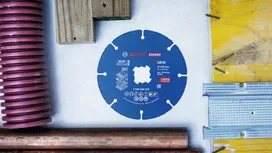Circular saw blade surrounded by metal pipes, wood, plastic tubing, and wall profiles.