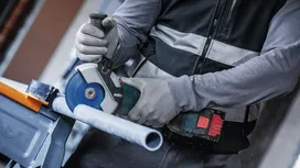 Person wearing safety equipment cuts a plastic pipe with a power tool.