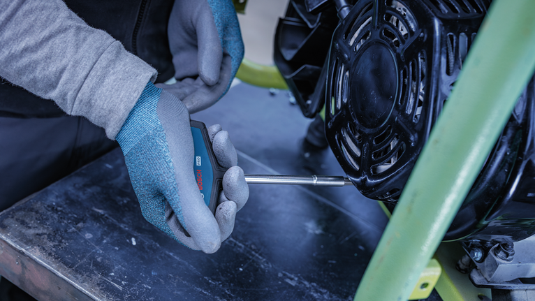 Person wearing safety equipment uses a screwdriver to adjust a machine part.