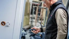 Person wearing safety equipment tightens a door hinge with a screwdriver.