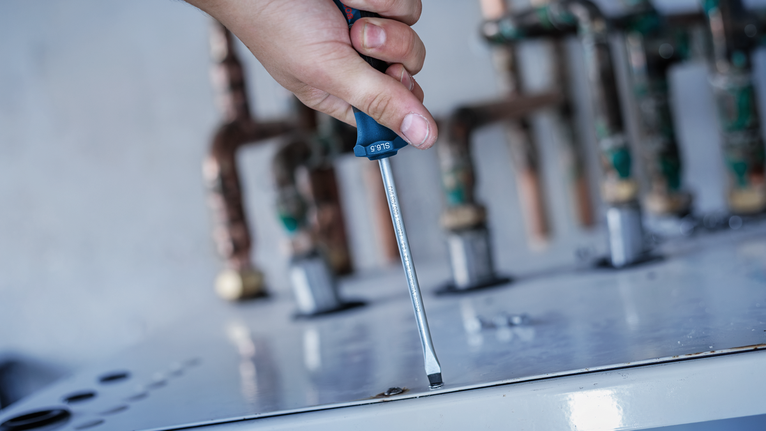 Person using a screwdriver to fasten a screw on a metal surface.