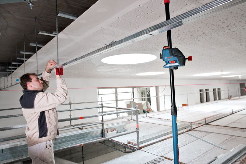 Person adjusts ceiling framework near a mounted laser leveling tool.