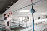 Person adjusts ceiling framework near a mounted laser leveling tool.