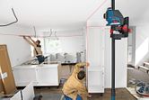 Two persons installing cabinets align shelves using a laser leveling tool.