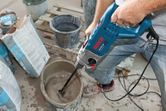 A person mixes construction material in a bucket using an impact drill.