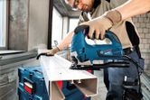 A person wearing safety equipment uses a jigsaw to cut a plastic channel.