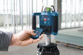 A person operates a laser leveling tool on a tripod inside a construction site.