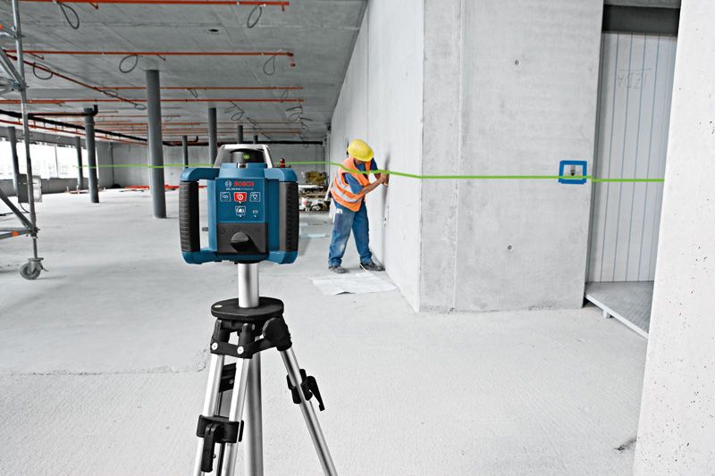 A person wearing safety equipment marks a wall using a green laser leveling tool.