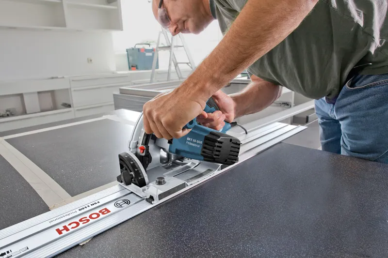 A person wearing safety equipment uses a plunge saw to cut a straight line in a panel.