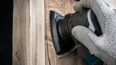 Ένα άτομο που φοράει εξοπλισμό ασφαλείας τρίβει ξύλο με ένα ηλεκτρικό εργαλείο.