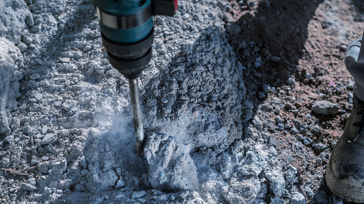 Κρουστικό τρυπάνι που σπάει τραχύ σκυρόδεμα, εργαζόμενος που φοράει εξοπλισμό ασφαλείας.