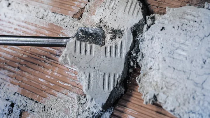 Σμίλη που αφαιρεί το αποξηραμένο κονίαμα από έναν τοίχο από τούβλα.