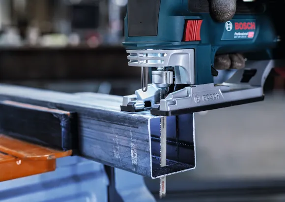 Άτομο που φοράει εξοπλισμό ασφαλείας κόβει μια μεταλλική δοκό με ένα παζλ.