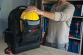 Σακίδιο πλάτης Bosch L-BOXX Contractor που κρατάει ένα κίτρινο σκληρό κράνος.