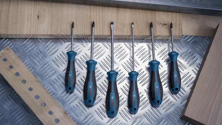 Έξι κατσαβίδια με μπλε και μαύρες λαβές τοποθετημένα σε μεταλλική επιφάνεια κοντά σε ξύλινα κομμάτια.
