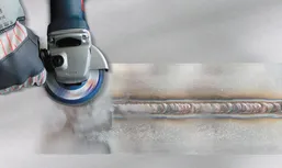 Radnik u zaštitnoj opremi brusi zavareni šav na metalu kutnom brusilicom.