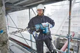 Osoba u zaštitnoj opremi buši beton velikim rotacijskim čekićem.