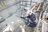 Osoba u zaštitnoj opremi buši beton velikim rotacijskim čekićem.