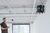 Osoba upravlja laserskim nivelmanom postavljenim na zid kako bi poravnala okvir stropa.