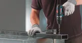Osoba koja nosi zaštitnu opremu buši metalnu gredu pomoću FlexiClick adaptera.
