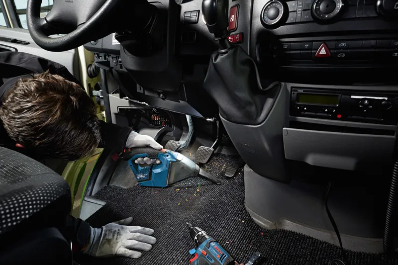 Osoba koja nosi zaštitnu opremu čisti pod automobila bežičnim usisavačem.