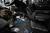 Osoba koja nosi zaštitnu opremu čisti pod automobila bežičnim usisavačem.