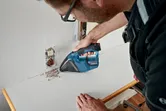 Osoba koja nosi zaštitnu opremu čisti otpad u blizini električne utičnice bežičnim usisavačem.
