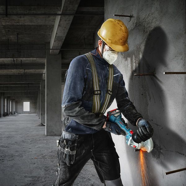 Osoba u zaštitnoj opremi reže beton kutnom brusilicom.