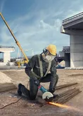 Osoba koja nosi zaštitnu opremu koristi kutnu brusilicu za rezanje metalnih šipki na gradilištu.