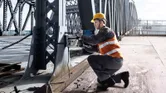 Osoba koja nosi zaštitnu opremu koristi magnetsku bušilicu na čeličnom mostu.