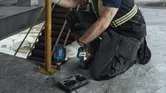 Osoba koja nosi zaštitnu opremu koristi bušilicu za pričvršćivanje metalnog stupa na betonski pod.