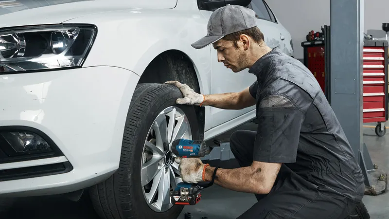 Osoba koja nosi zaštitnu opremu koristi udarni ključ za pričvršćivanje kotača automobila.